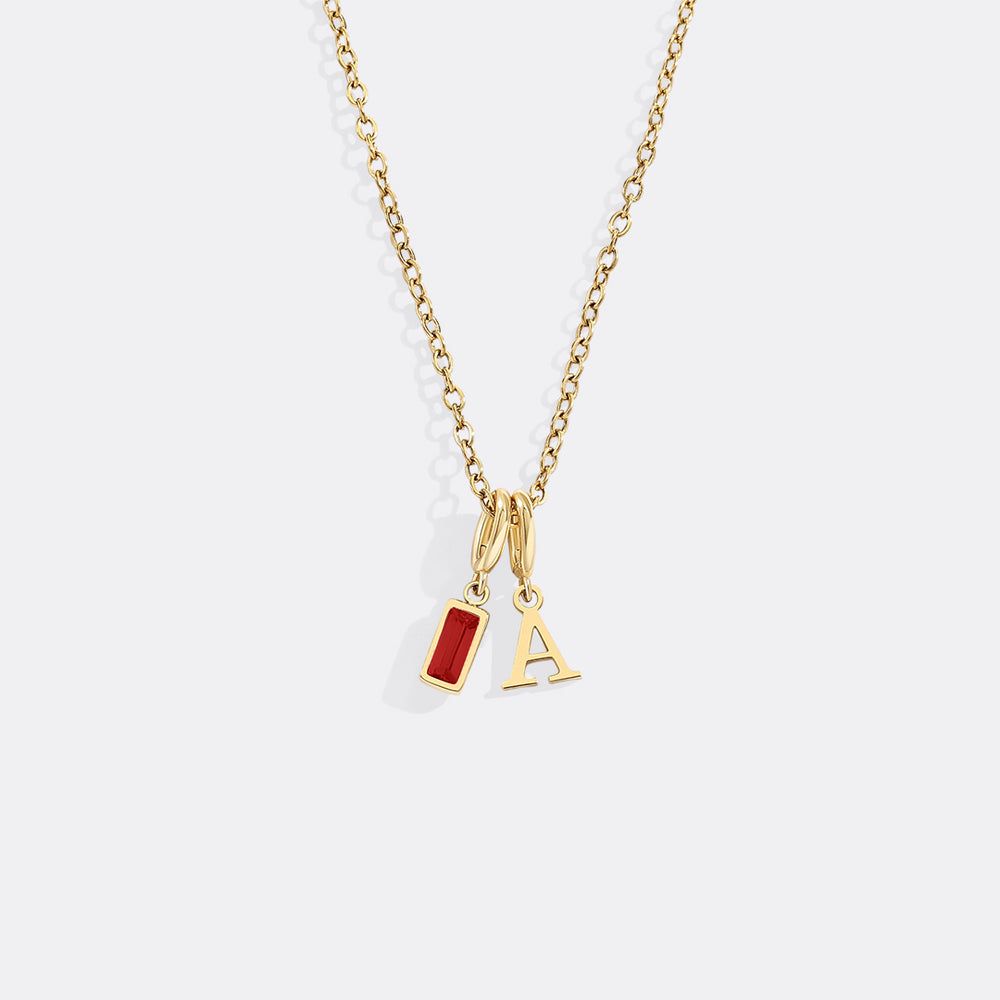 Gold necklace with red pendant and letter 'A' charm on a white background