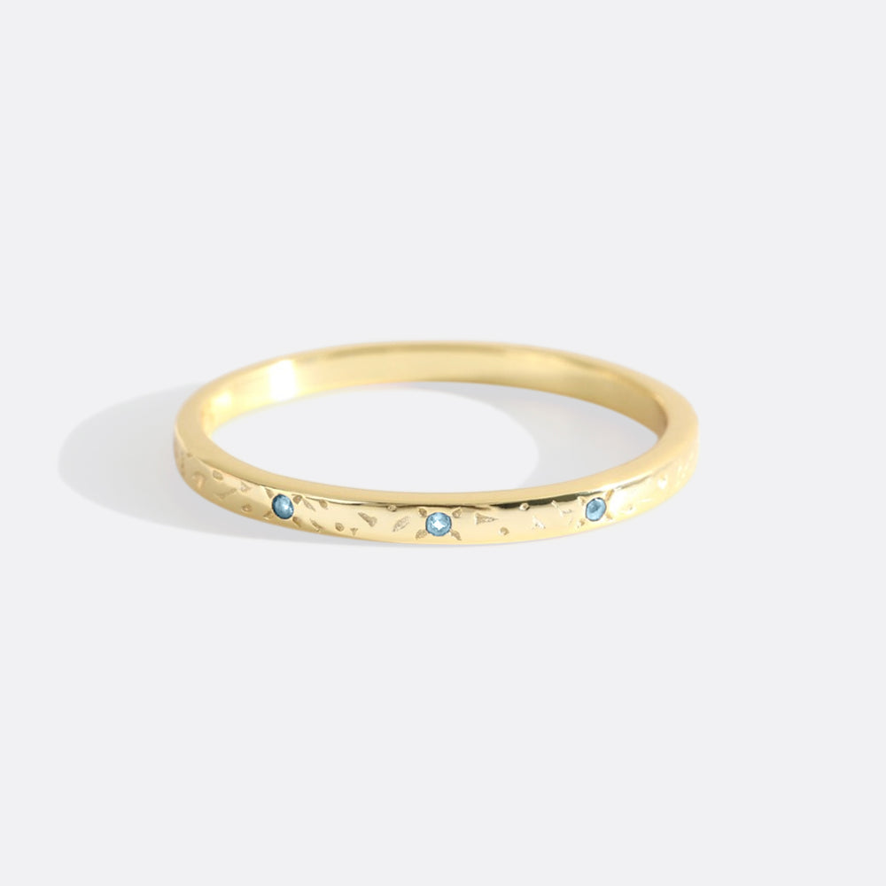 A thin gold band with red birthstones set at intervals along its length, displayed against a white background.