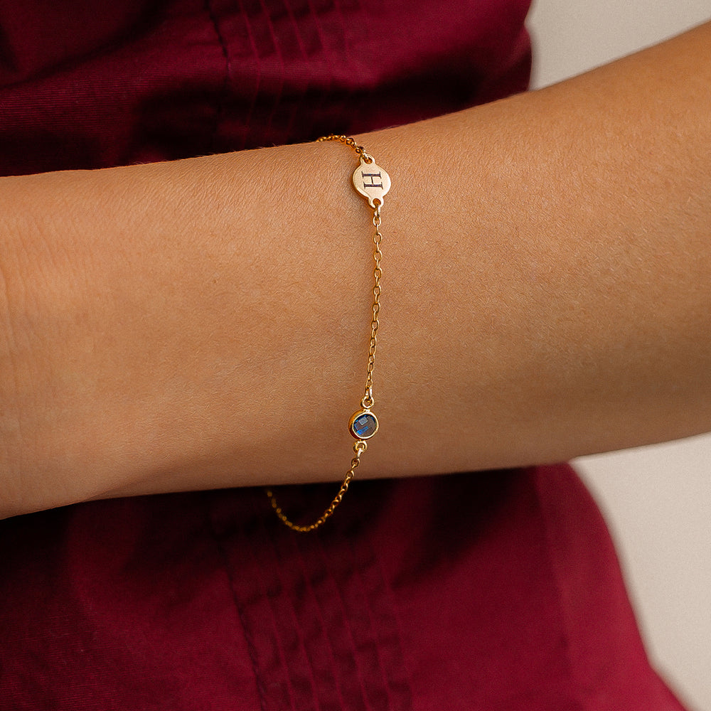 Gold bracelet with a blue gemstone on a wrist against a red fabric background