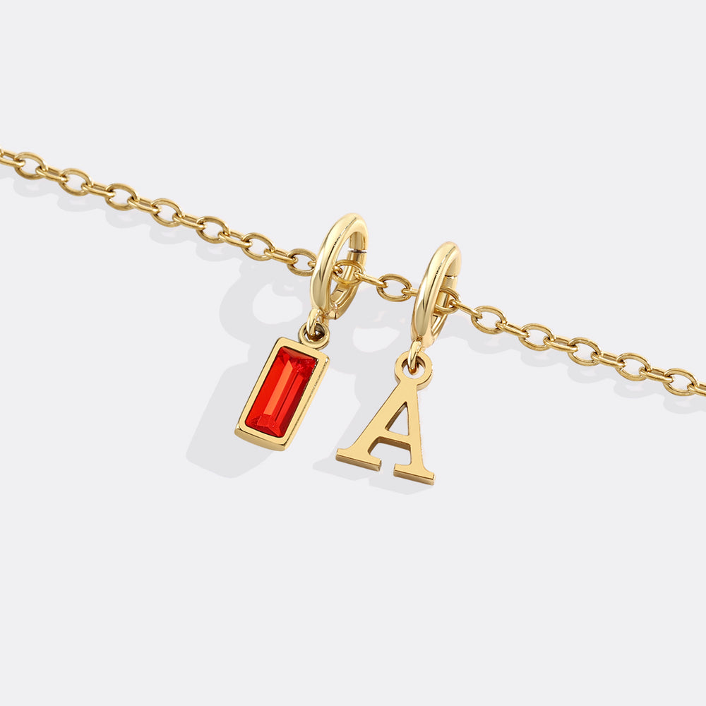 Gold necklace with a red pendant and letter 'A' charm on a white background