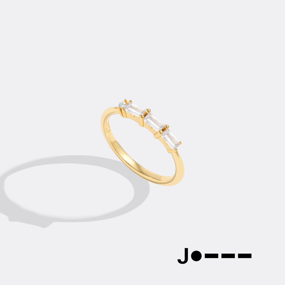 Gold ring with clear gemstones on a white background, featuring the brand 'Jo--'.