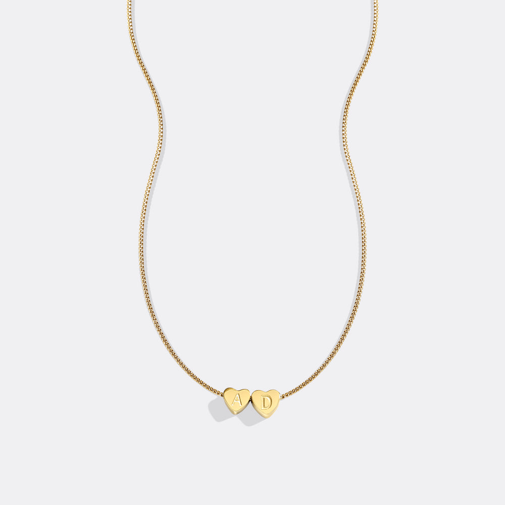 Gold necklace with heart-shaped pendants on a light gray background