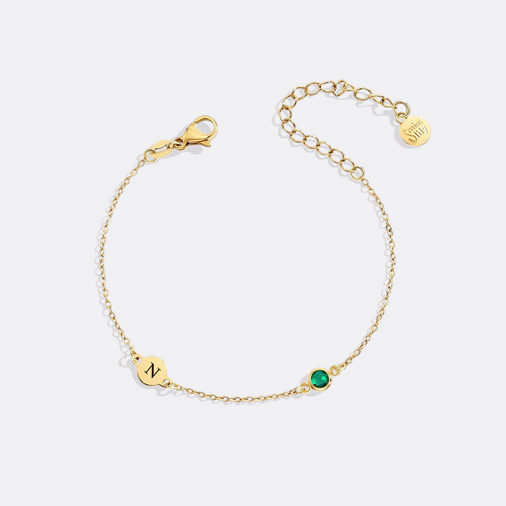 Gold bracelet with a green gemstone and 'N' charm on a white background