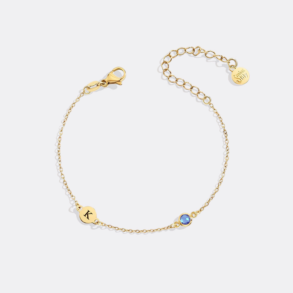 Gold bracelet with a blue gemstone and 'K' charm on a white background