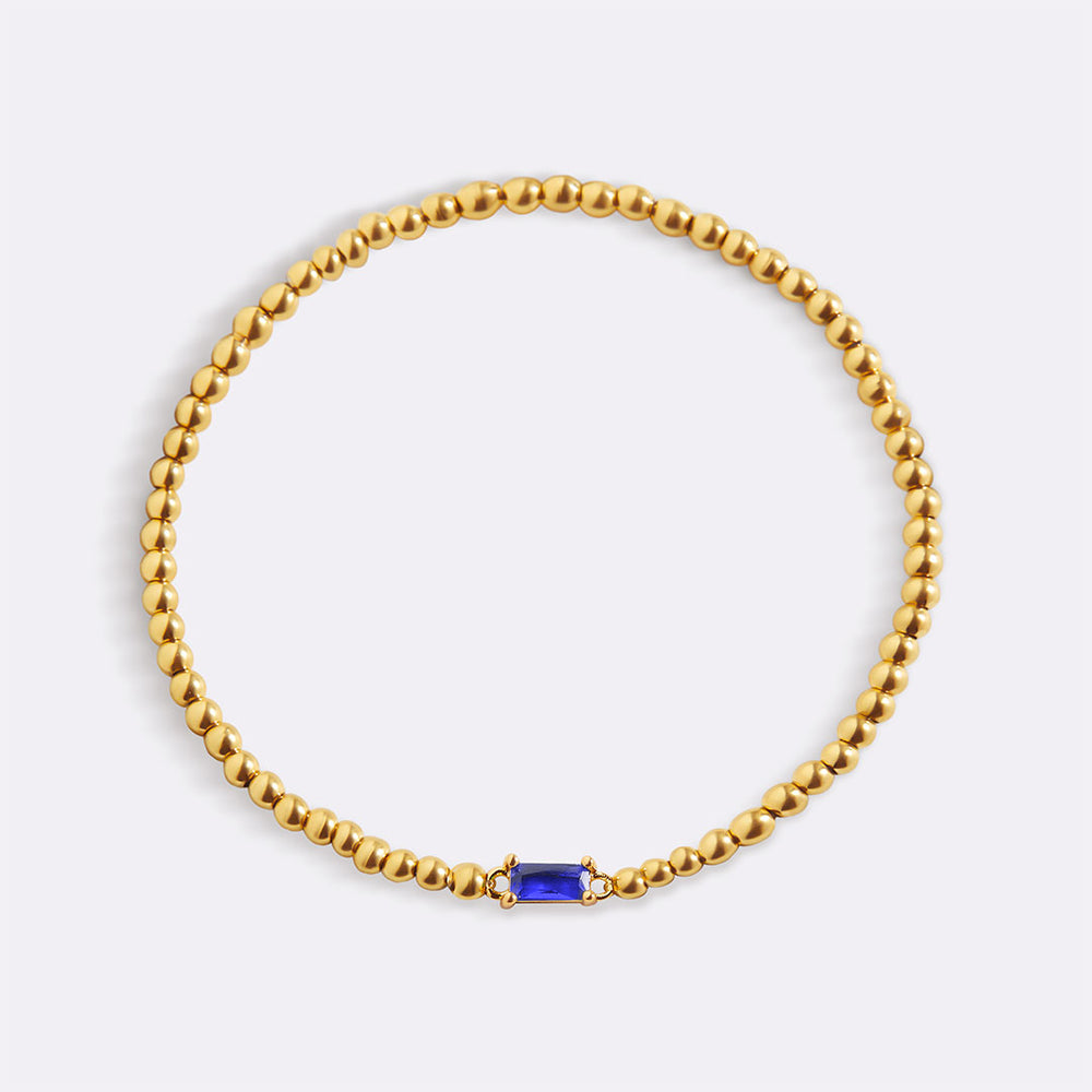A gold vermeil bracelet with beaded design and a red birthstone charm.