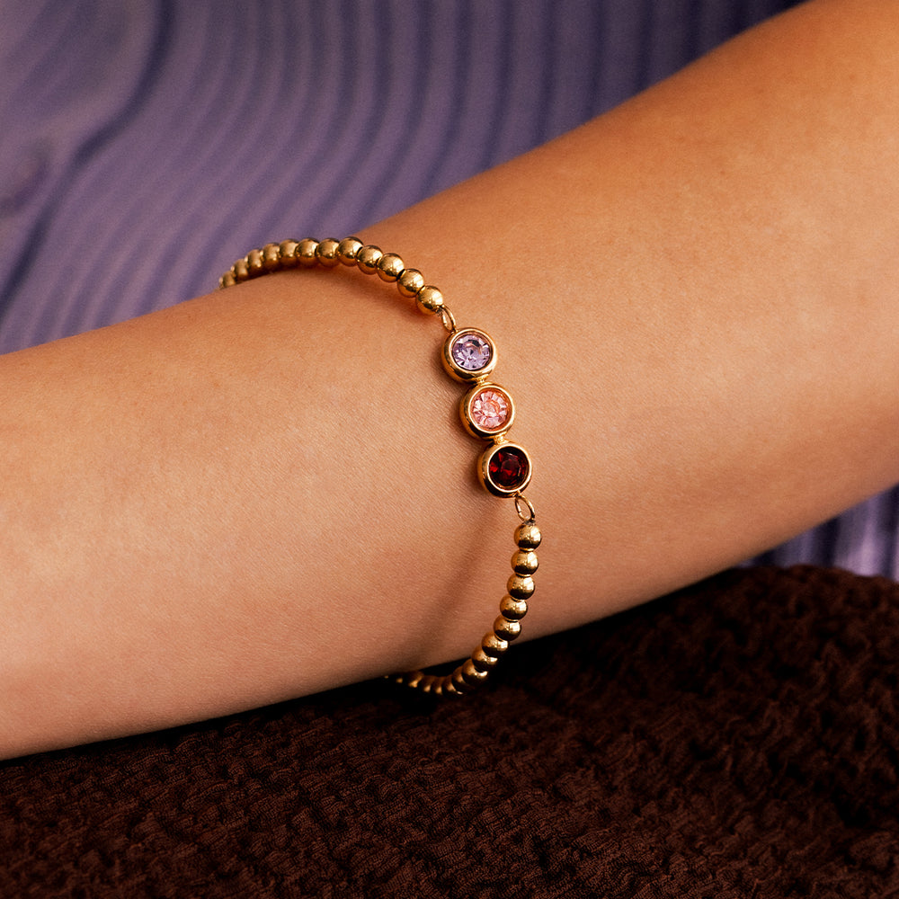Gold bracelet with gemstones on a wrist against a textured purple and brown background