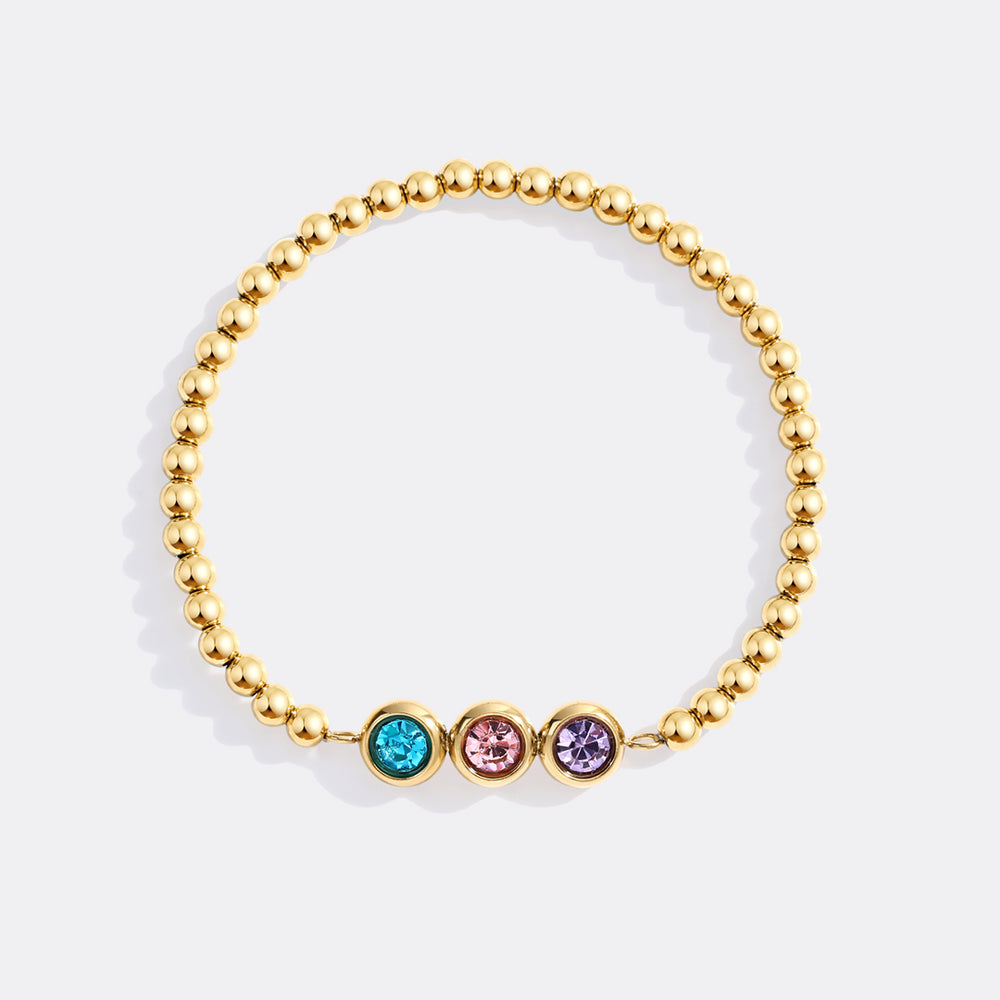 Gold beaded bracelet with three colored gemstones on a light gray background
