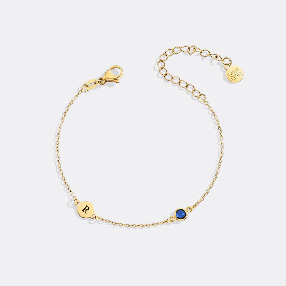 Gold bracelet with a blue gemstone and 'R' charm on a white background