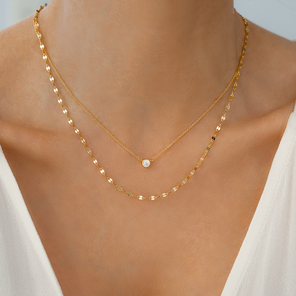 Gold necklace with a small round pendant on a person wearing a white top.