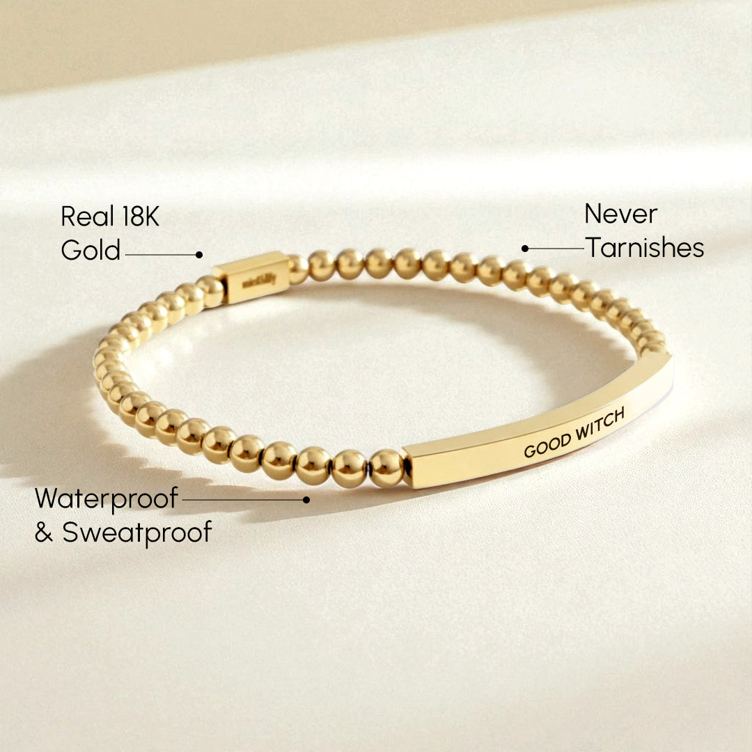 Gold bracelet with 'GOOD WITCH' engraving on a beige background