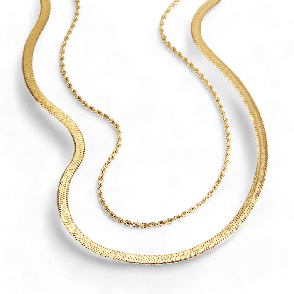 Two layered gold-colored necklaces, one with a herringbone pattern and the other with a rope texture, displayed against a black background.