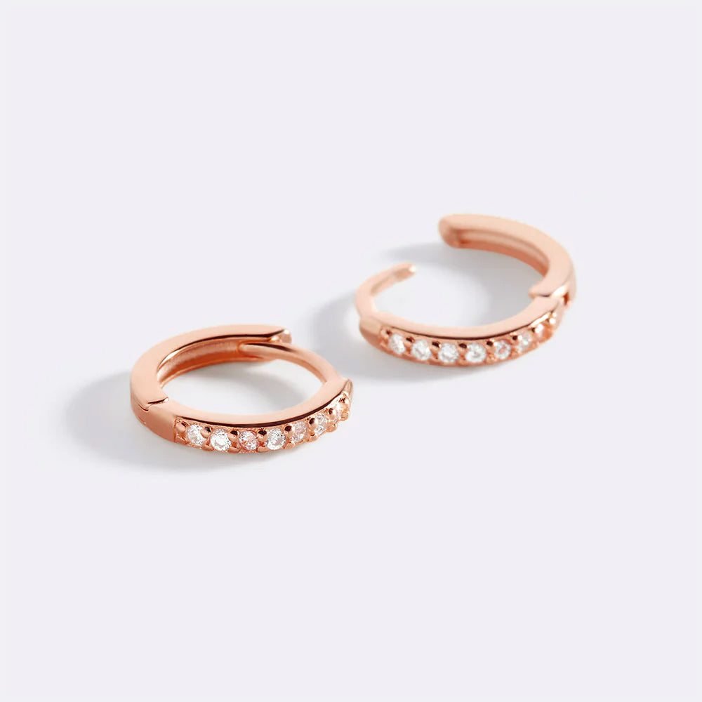 Rose gold hoop earrings with embedded stones on a light gray background