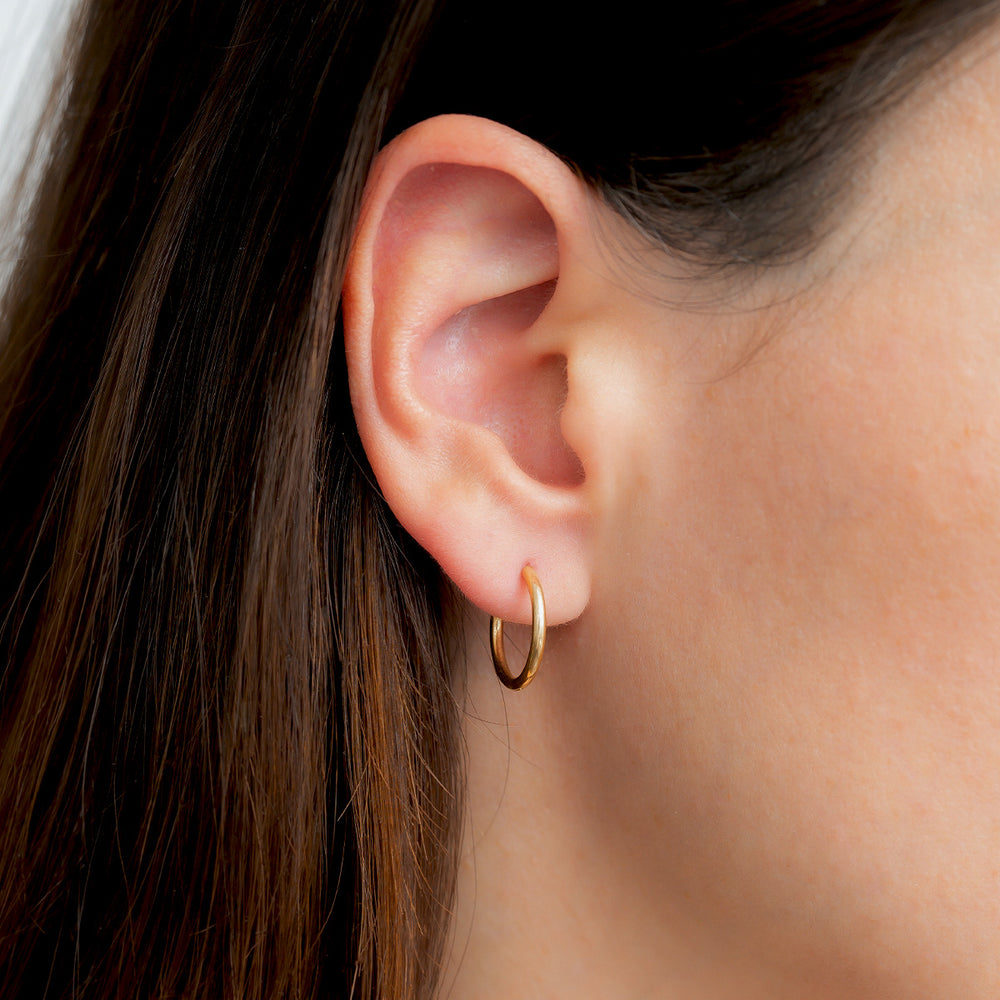 Close-up of an ear wearing a gold hoop earring with dark hair.
